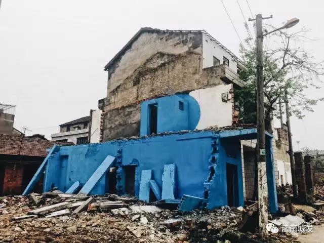 △ 這棟建筑是臨江最近的半拆遷建筑物的遺留，沅江和堤壩成為了展覽的天然背景。創(chuàng)作團(tuán)隊(duì)對(duì)這棟建筑進(jìn)行了半涂裝，將符號(hào)性的沅水曲線與拆遷進(jìn)行中的建筑立面進(jìn)行意義的疊造，它們共同觸發(fā)了場(chǎng)所空間多元語(yǔ)境的生成，把拆遷這種暫時(shí)破壞性、干擾性的介入行動(dòng)與沅水右岸發(fā)展的未來(lái)性、美好性緊密融合。